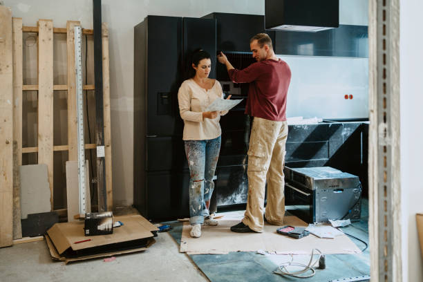 couple discussing over document while fixing cabinet together in kitchen during home renovation - home decoration stock pictures, royalty-free photos & images