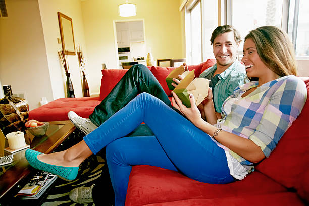 couple eating take out food on sofa - junk food stock pictures, royalty-free photos & images