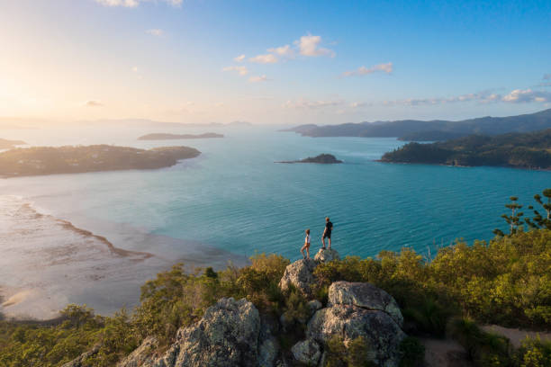 couple enjoying the view on top mountain overlooking whitsundays ocean - travel stock pictures, royalty-free photos & images