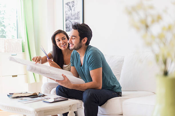couple examining blueprints in living room - home decoration stock pictures, royalty-free photos & images