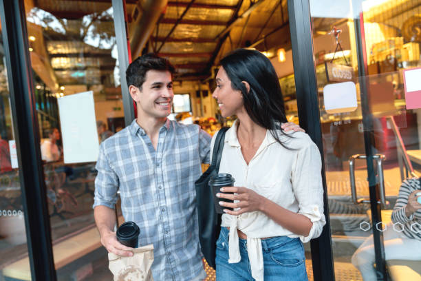 couple exiting a cafe carrying coffee to go - junk food stock pictures, royalty-free photos & images