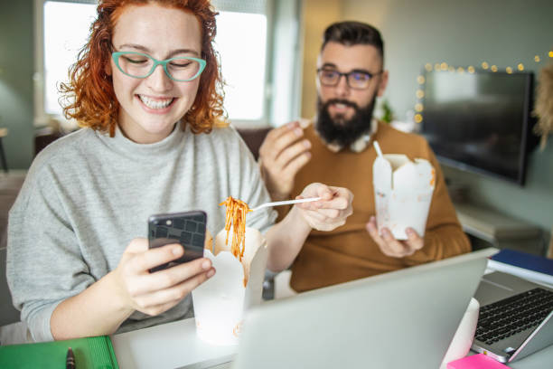 couple is taking a lunch break while working from home and eating fast food - junk food stock pictures, royalty-free photos & images