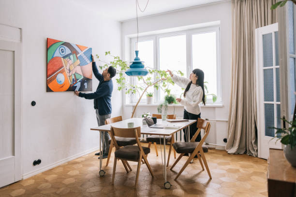 couple looking for perfect place to hang their painting - home decoration stock pictures, royalty-free photos & images