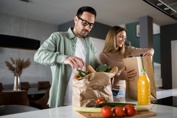 couple returning home from shopping trip and unpacking grocery bags - food stock pictures, royalty-free photos & images