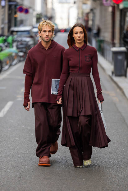 Couple Sebastien Roques wears burgundy shirt, pants & Alice Barbier wears pleated skirt, white bag, zipper outside Lacoste during Womenswear...