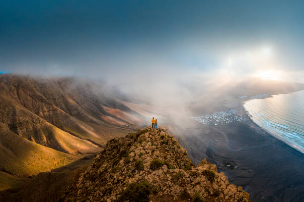 couple standing on top of a cliff looking at sunset, lanzarote, spain - travel stock pictures, royalty-free photos & images