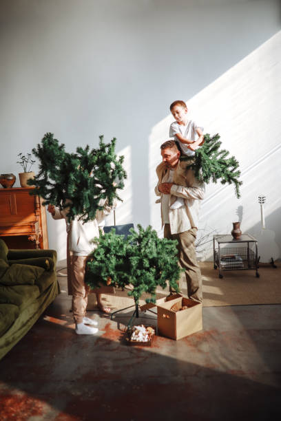 cozy christmas: parents and sons assemble the tree in a minimalist eco-friendly interior together - home decoration stock pictures, royalty-free photos & images