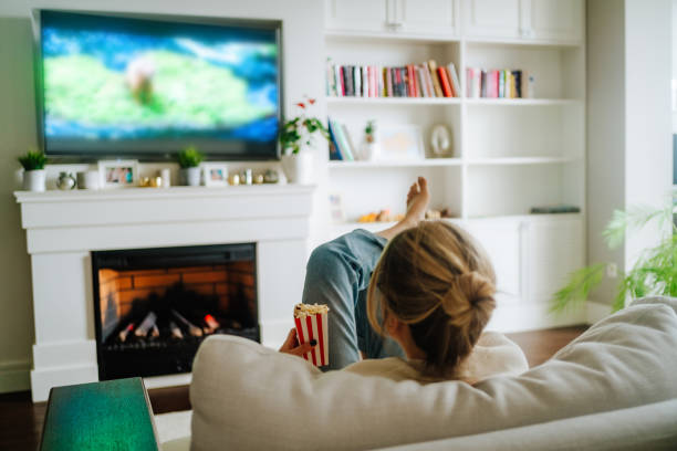 cozy hugge fireplace and watching tv. woman eating popcorn and watching tv on a big screen at home - junk food stock pictures, royalty-free photos & images