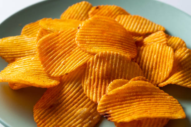 crispy fried potato chips in a bright ceramic bowl or plate, on a white background or table. corn spicy fatty chips with paprika and spices. the concept of unhealthy diet and lifestyle, accumulation of excess weight. copy spa