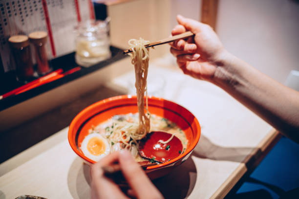 cropped hand of woman eating a bowl of freshly served traditional japanese ramen with chopsticks in a japanese restaurant. asian cuisine and food culture. eating out lifestyle - food stock-fotos und bilder