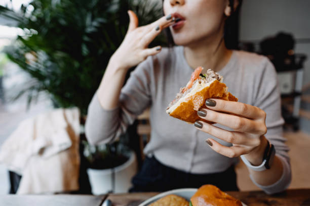 cropped shot, mid-section of young asian woman eating freshly made delicious cheeseburger in a cafe, licking her fingers. enjoying her lunch! people and food concept - junk food stock pictures, royalty-free photos & images