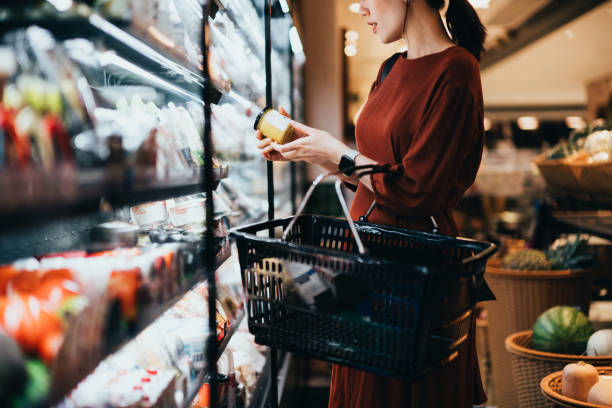 cropped shot of young asian woman carrying a shopping basket, standing along the dairy aisle, reading the nutrition label on the bottle of a fresh organic healthy yoghurt. making healthier food choices - food stock pictures, 