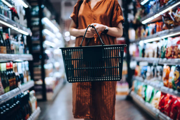 cropped shot of young woman carrying a shopping basket, standing along the product aisle, grocery shopping for daily necessities in supermarket - food stock pictures, royalty-free photos & images