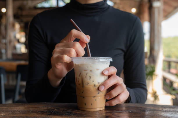 cropped shot view of asian woman holding a plastic cup of iced milk coffee before drink. - junk food stock pictures, royalty-free photos & images