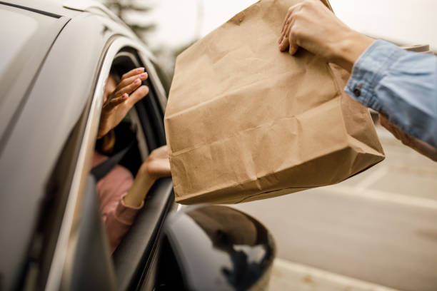 customer receiving coffee and takeaway food order from a service person at the drive through - junk food stock pictures, royalty-free photos & images