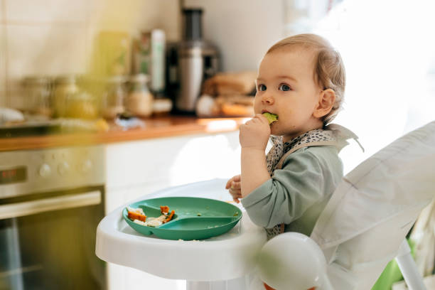 cute baby girl eating meal at high chair - food stock pictures, royalty-free photos & images