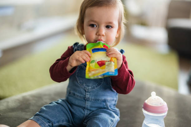 cute little girl eating fruit puree in pouch - food stock pictures, royalty-free photos & images