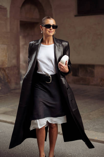 Darja Barannik wears grey and white midi skirt, white top, black long leather coat, black leather belt, white bag, sunglasses outside the Rotate show...