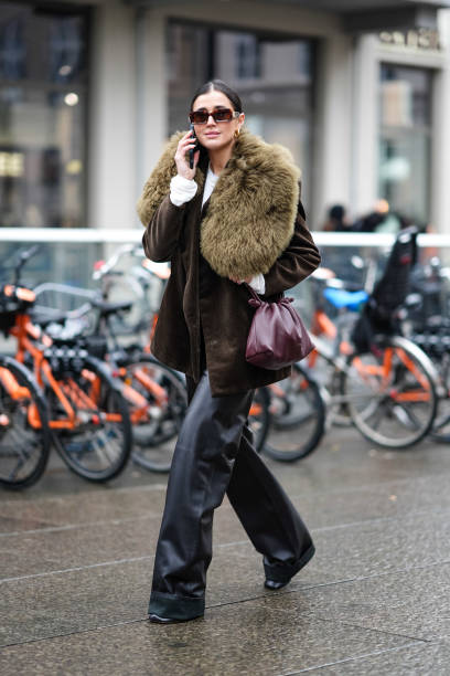 Darja Barannik wears sunglasses, a brown and khaki jacket with fluffy oversized parts at lapel and collar levels, a purple leather bag, black leather...