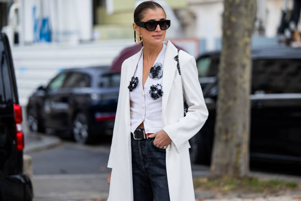 Darja Barannik wears white coat, blouse, sunglasses dark denim jeans, black bag, golden earrings outside Chanel during the Womenswear Spring/Summer...