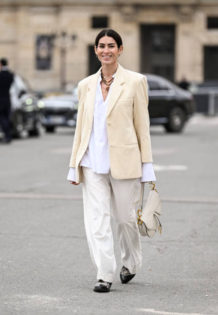 Deborah Reyner Sebag is seen wearing a cream jacket, white button down shirt, white pants, black shoes and black sunglasses outside the Dior show...