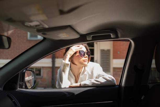 delightful woman standing near automobile, leaning on open window, softly touching forehead and looking away through classy sunglasses, posing on backdrop of city buildings. - fashion stock pictures, royalty-free photos & ima