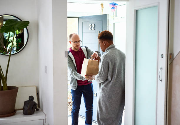 delivery man handing take away to woman at front door - junk food stock pictures, royalty-free photos & images