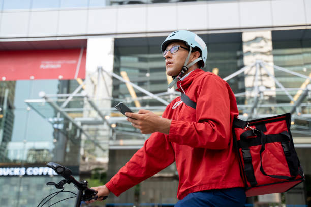delivery man pushing bicycle and checking directions on smartphone - junk food stock pictures, royalty-free photos & images