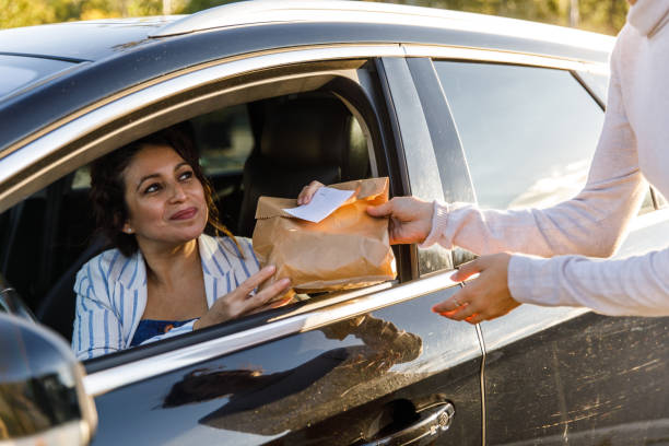 delivery woman at the curbside pickup giving takeaway order to a customer - junk food stock pictures, royalty-free photos & images