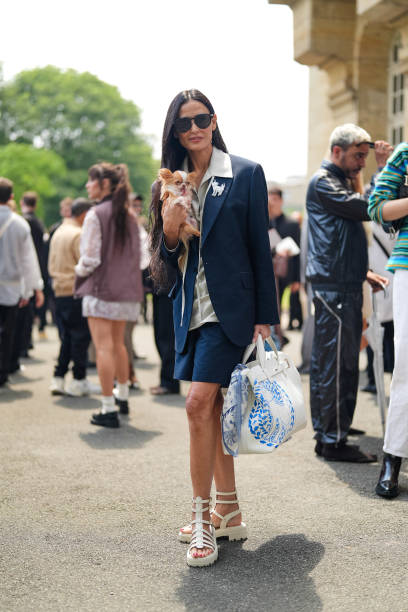 Demi Moore wears black sunglasses, silver necklace, gray v-neck oversized shirt, black oversized blazer jacket, black mini skirt, white striped...