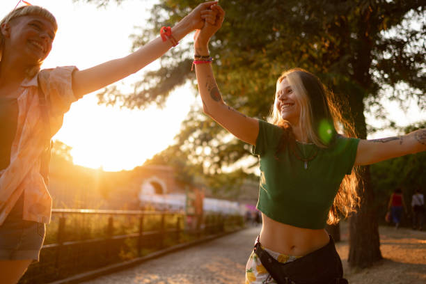 des femmes insouciantes se tenant la main lors d’un festival de musique au coucher du soleil. - concert photos et images de collection