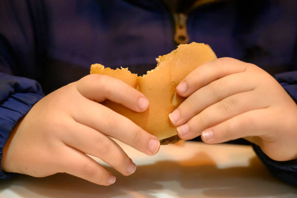 detail of a little boy's hands eating a hamburger. fast food. - junk food stock pictures, royalty-free photos & images