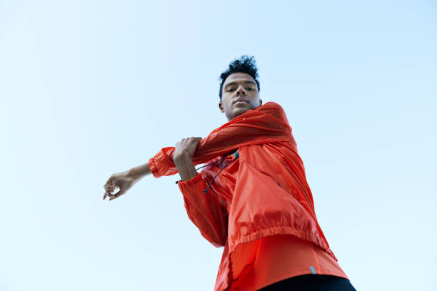 directly below portrait of athlete stretching arm against clear sky - fashion stock-fotos und bilder