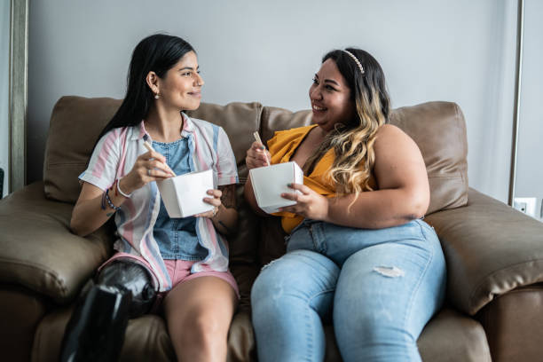 disabled mid adult woman eating yakisoba with her friend in the living room at home - junk food stock pictures, royalty-free photos & images