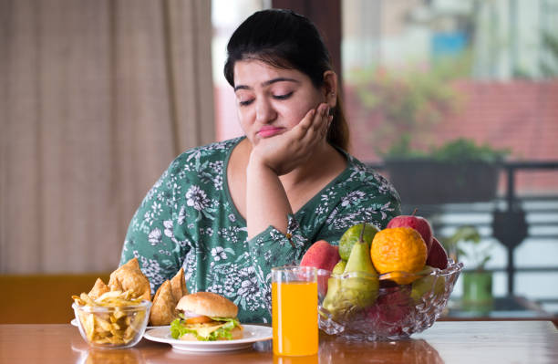 displeased woman with unhealthy and healthy food on table - junk food stock pictures, royalty-free photos & images