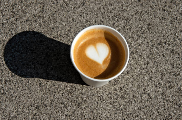 disposable cardboard cup of flat white coffee, with heart shape latte art, on a concrete pavement - junk food stock pictures, royalty-free photos & images