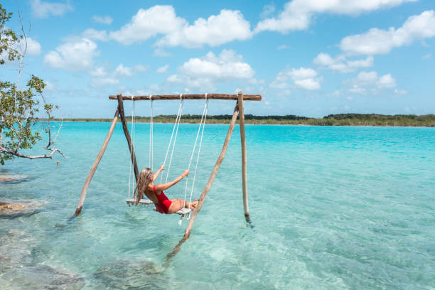 drone view of young woman having fun on swing in a beautiful lagoon on a sunny day - travel stock pictures, royalty-free photos & images