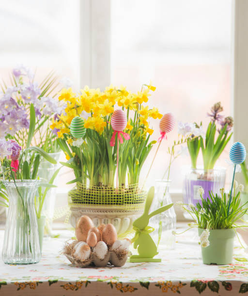 easter decoration with seasonal colorful potted flowers, easter eggs and bunny on table at window with natural light - home decoration stock pictures, royalty-free photos & images