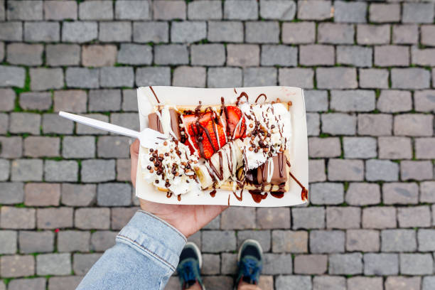 eating belgian waffle with sweet toppings and fresh fruits at the town square, personal perspective view - junk food stock pictures, royalty-free photos & images