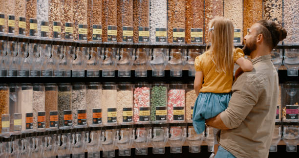 einkaufen, auswahl und vater mit kind wählt snacks und lebensmittel in einem supermarkt. einzelhandelsgeschäft, geschäft und vater und tochter pflücken süßigkeiten, süßigkeiten oder nüsse für ernährung und diät zum kaufen - j