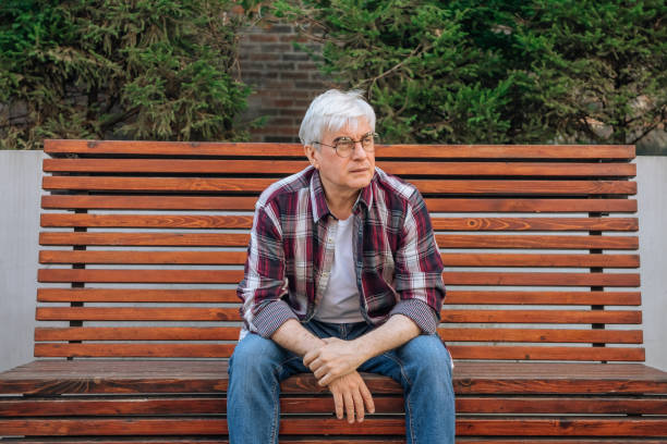 elderly man in glasses with gray hair sitting on a bench - garden decoration photos et images de collection