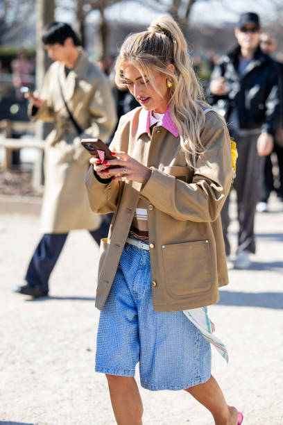 Emili Sindlev on the phone wears beige jacket, denim jeans shorts, striped brown polo outside Casablanca during the Womenswear Fall/Winter 2025/2026...
