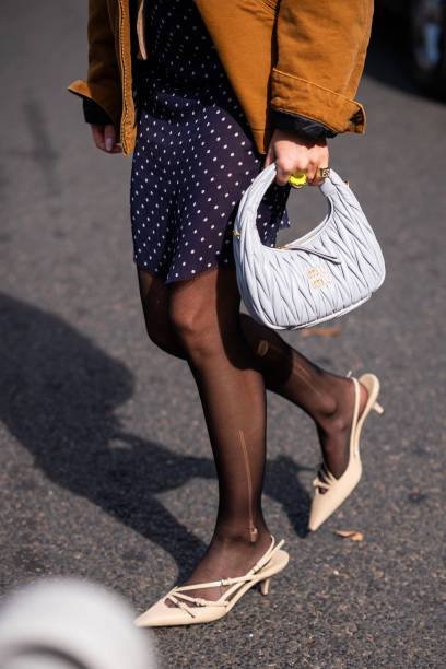 Emili Sindlev wears a beige top and cardigan, blue polka dot mini skirt, brown Carhartt jacket, gret Miu Miu bag and beige kitten heels, outside Miu...