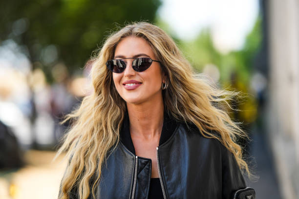 Emili Sindlev wears black sunglasses, a black shiny leather oversized bomber coat from Prada, a black shoulder-off cropped top, outside the Prada...