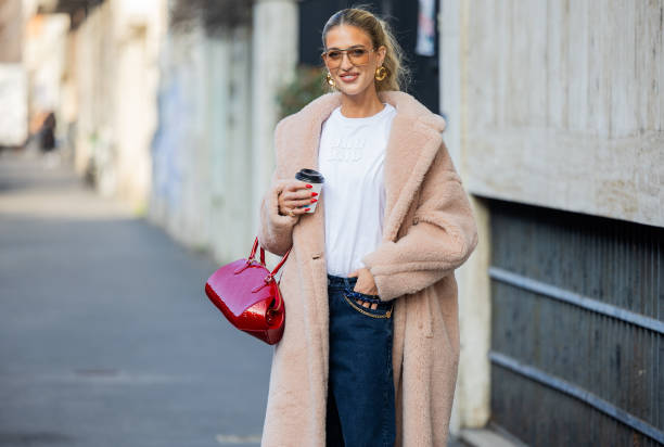 Emili Sindlev wears salmon colored coat, white Miu Miu shirt, sunglasses, golden earrings, red Louis Vuitton bag, denim jeans outside Max Mara during...