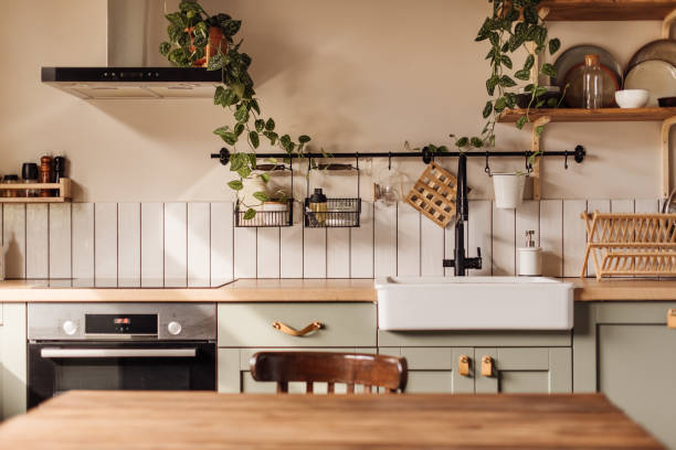 empty kitchen island with marble surface in foreground, green vintage countertop with drawers and pendant lights hanging above, lots of flowers in jars, blurred background - home decoration stock pictures, royalty-free photos