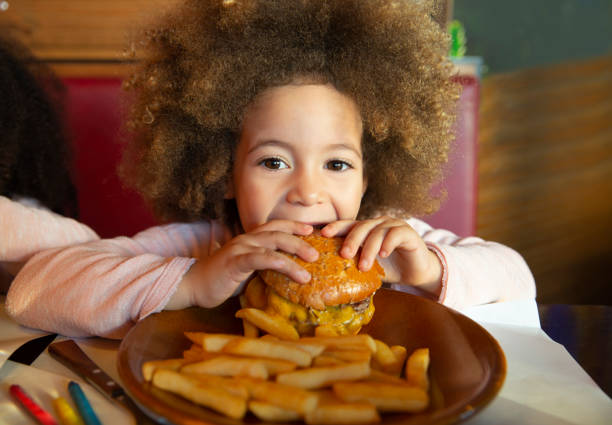 ethnic kid girl eating burger and chips - junk food stock pictures, royalty-free photos & images