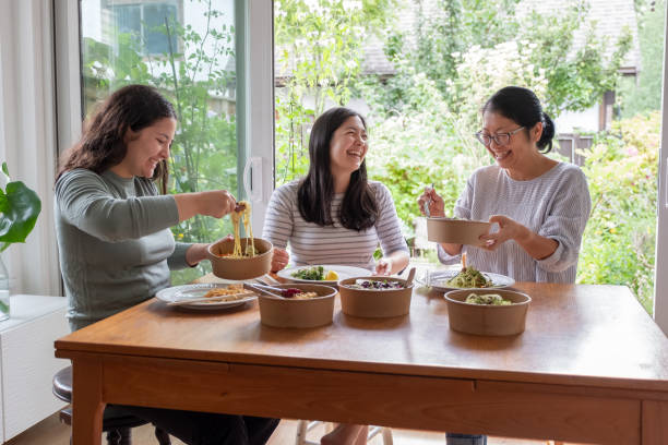 eurasian daughters and chinese mother eating vegan takeout meal together - junk food stock pictures, royalty-free photos & images