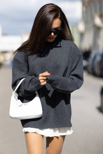 Evangelie Smyrniotaki is seen wearing black sunglasses, a white Prada bag, a grey oversized long sleeves sweater and a white mini skirt outside the...