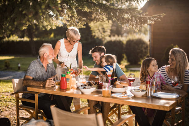 famille élargie heureuse parlant tout en ayant leur déjeuner dans la cour avant. - garden decoration photos et images de collection